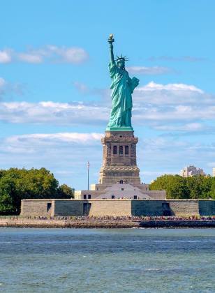 Die Freiheitsstatue in New York. Es ist eine türkise Statue einer Frau die ein Buch und eine Fackel hält.